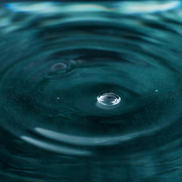 Clear water droplet creating ripples on a calm surface.